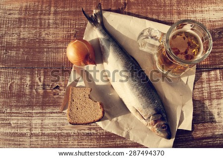 Beer in a glass, a salty herring on paper, bread and onions on a structural wooden table. Beer and snack to beer.