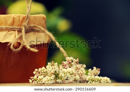 Honey in a glass jar with flowers of a buckwheat  in a summer sunny day. Honey with flower close up