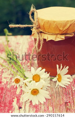 Honey in a glass jar and field camomiles on the old painted wooden surface.