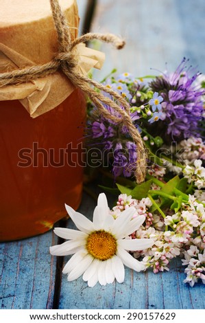 Honey in a glass jar with June flowers melliferous herbson a blue wooden surface. Honey with flowers