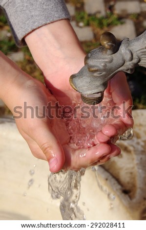 Child gathers in hands water from under the crane. Water and children's hands
