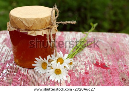 Honey in a glass jar and field camomiles on the old painted wooden surface.