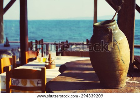 Clay Greek vase against coastal cafe and the sea. Coastal cafe.