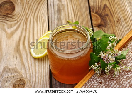 Honey in a glass jar, buckwheat flowers, a lemon and bee honeycombs in a summer sunny day. Honey with flowers and honeycombs