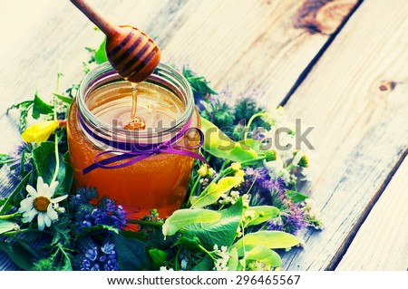 Honey in a glass jar the tied gift tape with a bow with June flowers melliferous herbson a wooden surface. Honey with flowers