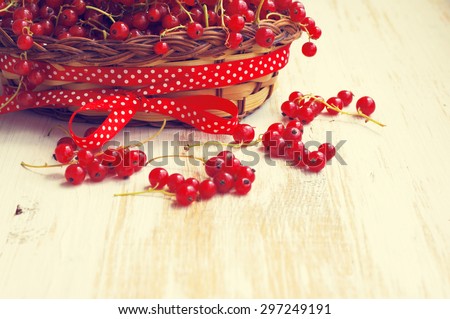 Berries of red currant in the basket decorated with a red tape on a wooden light background. Wooden basket with fresh red currants