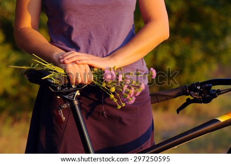 Girl\'s hands with a bouquet of wild flowers by bicycle. Girl with flowers and the bicycle