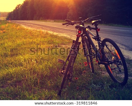 Two road bicycles nearby with each other near the road. Romantic couple of bicycles against the leaving sun