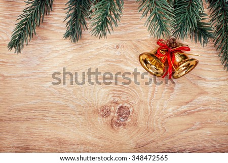 Gold Christmas bells and fir tree branch on a rustic wooden background. Xmas card. Happy New Year. Top view with copy space