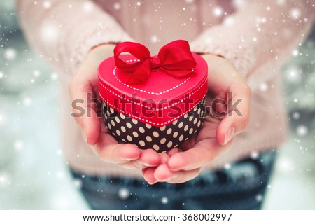 Female hands holding a gift box shaped of heart. The Valentines day and Christmas theme