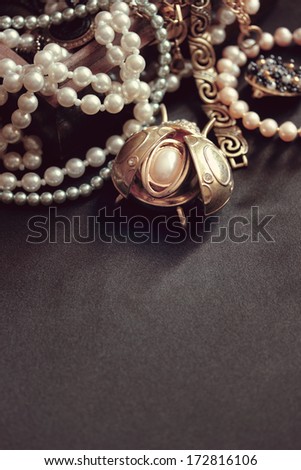 art vintage golden and pearl bijouterie with scarab on black silk background in sepia and peach; vertical card