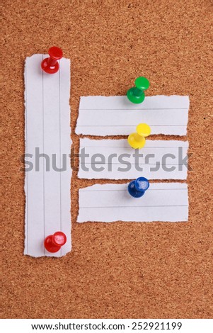 Some pieces of blank note paper are pinned to a cork board.