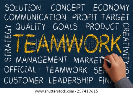 Teamwork word cloud is written on blue chalkboard by the hand of a businessman.