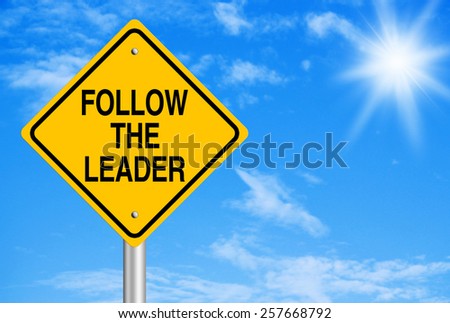 Follow the leader text is on road sign with blue sky background.