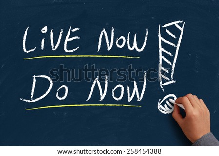 Live now do now on blue chalkboard with the hand of businessman.