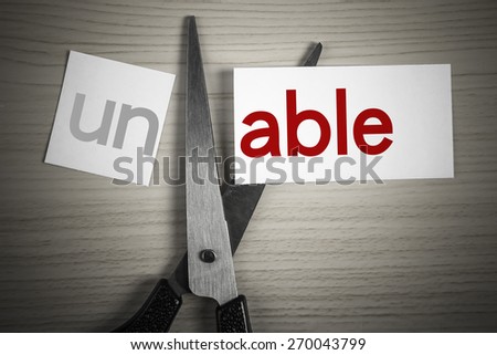 A scissor cuts able from unable on the desk.