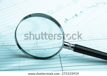 Magnifying glass is lying on the paper with financial graph.