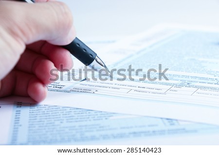 A person is completing the tax form with a pen.
