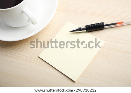 Blank sticky note is on the table with ball pen and coffee aside.