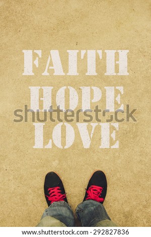 Faith hope love text is painted on the ground in front of the feet.