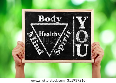 Hands holding blackboard with text You Body Spirit Soul Mind Healthy against green blurred background.