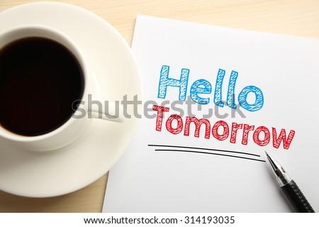 Text Hello Tomorrow written on the white paper with pen and a cup of coffee aside.