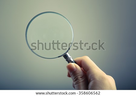 Hand holding a magnifying glass with blank background.
