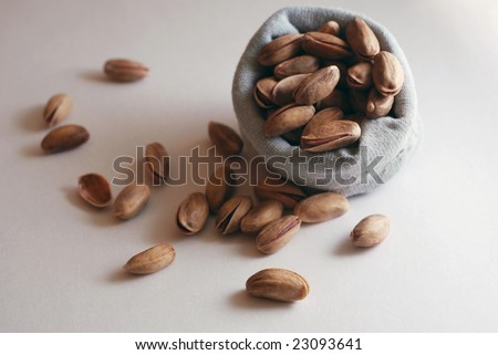 Pistachio nuts falling out of  small bag on white table. For other similar images from the series, please, check my portfolio.