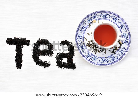 Word tea written with black tea leaves and a cup of tea