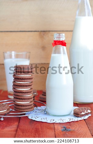 Milk in a bottle with a red bow and chocolate cookies on a red wooden background.