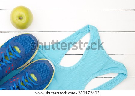 Old sport shoes, shirt and apple on a white wooden background. Sport equipment top view