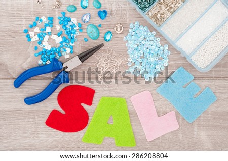 Crystals, pendants, charms, plier, glass hearts, box with beads, accessories to create hand made jewelry and inscription sale of felt on old wooden background. Top view. Selective focus
