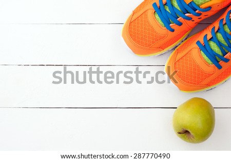 Sport shoes sneakers and apple on white wooden background. Top view sport equipment. Selective focus