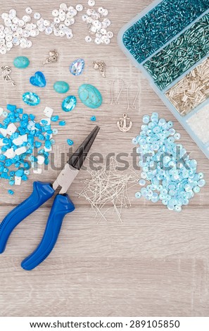 Tools for making jewellery. Crystals, pendants, charms, plier, glass hearts, box with beads and accessories on old wooden background. Top view
