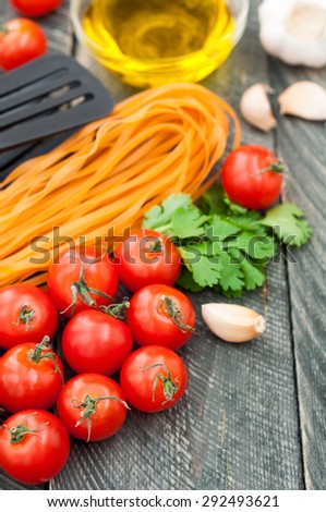 Cherry tomatoes, pasta, olive oil, garlic, herbs and pasta tongs on the old wooden background. Rustic style. Italian food. Selective focus