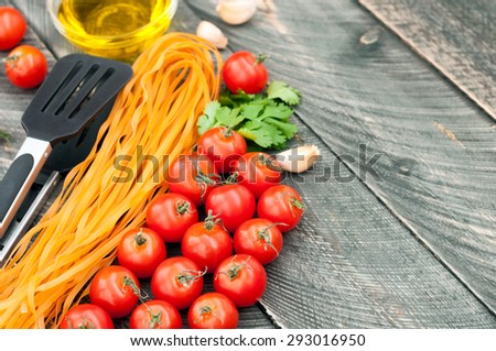 Cherry tomatoes, pasta, olive oil, garlic, herbs and pasta tongs on the old wooden background. Rustic style. Italian food. Selective focus