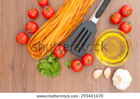 Cherry tomatoes, pasta, olive oil, garlic, herbs and pasta tongs on the old wooden background. Rustic style. Italian food. Top view