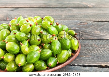 Fresh wet gooseberries on a plate on a wooden background. Green gooseberry closeup. Rustic style