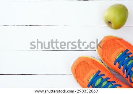 Orange sport shoes sneakers and apple on white wooden background. Top view sport equipment.