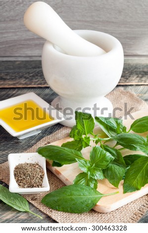 The leaves of fresh basil on a chopping board, olive oil, dried basil spices and mortar on a wooden table. Rustic style. Selective focus
