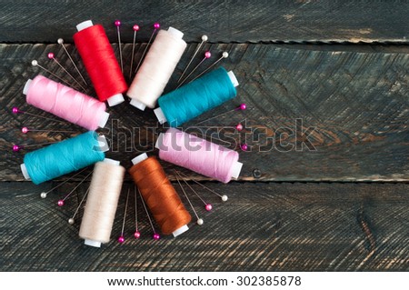 Spools with different colors of thread and pins on old wooden background. Sewing accessories. Top view