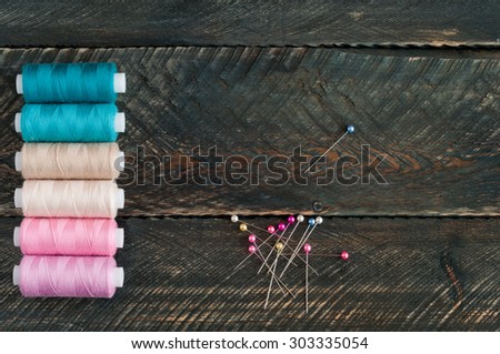Spools of thread and pins on old wooden background. Sewing accessories. Top view