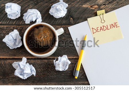 Sticky note with the word deadline. White blank paper, crumpled paper, pen and a cup of coffee on a wooden background