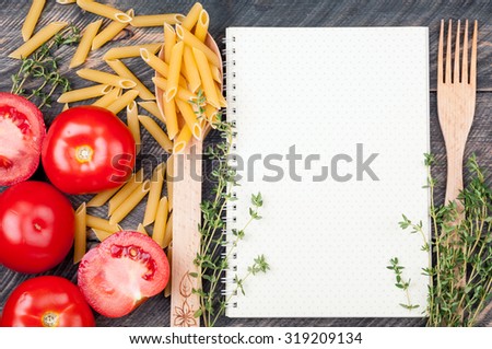 Open sheet cookbook with pattern polka dot, spoon with penne pasta, tomatoes, thyme on old wooden background. Ingredients for cooking. Open blank recipe book. Top view