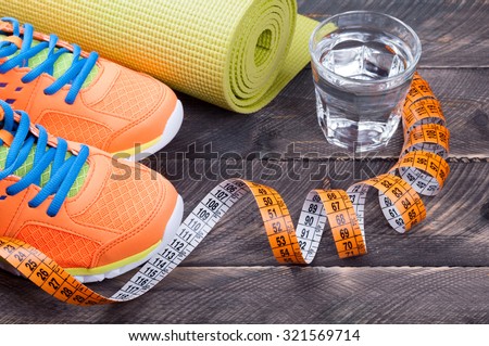 Sport shoes, yoga mat,  glass of water and centimeter on wooden background. Sport equipment. Concept healthy life. Selective focus