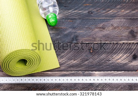 Yoga mat, water bottle and centimeter on a wooden background. Equipment for yoga. Concept  healthy lifestyle. Selective focus