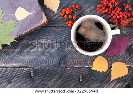 Coffee cup with foam, old book, autumn leaves and dried rowan on wooden background. Concept cozy atmosphere with a cup of coffee. Copy space. Autumn card. Top view