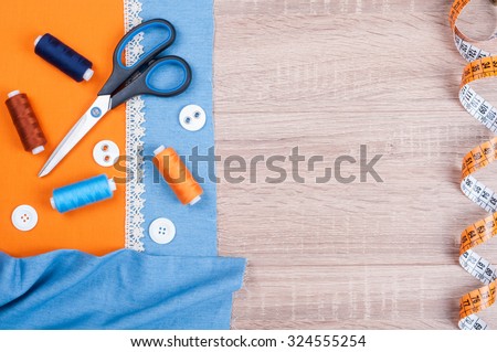 Jeans and cotton fabrics for sewing, lace, measuring tape and accessories for needlework on wooden background. Spool of thread, scissors, buttons, sewing supplies. Set for needlework top view