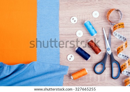 Set for needlework top view. Jeans and cotton fabrics for sewing, spool of thread, scissors, buttons, measuring tape and accessories for needlework on old wooden background