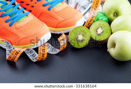 Sport shoes, fruits,  bottle of water and measuring tape on dark background. Sport equipment. Concept healthy life, sports and diet. Selective focus